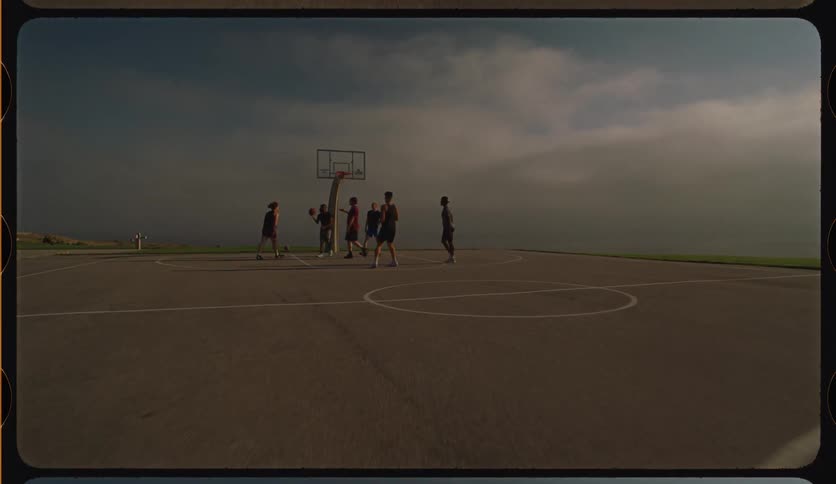 A group of friends plays a casual game of basketball on an outdoor court with a vintage film aesthetic as the camera slowly pushes in