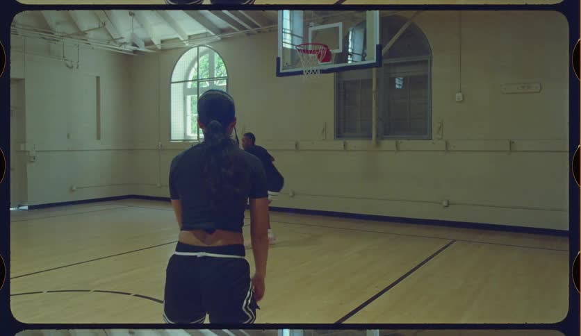 Two women in athletic wear practice shooting hoops in slow motion on an indoor basketball court