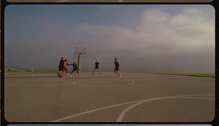 Slow-motion, vintage-style shot of a diverse group of young men playing basketball on an outdoor court against a hazy sky
