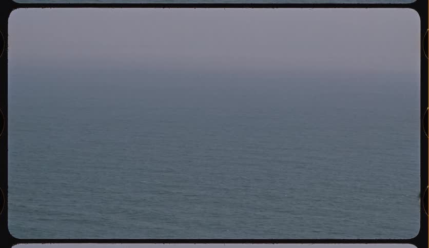 Vintage film footage shows a calm, vast ocean blending into a foggy, overcast sky