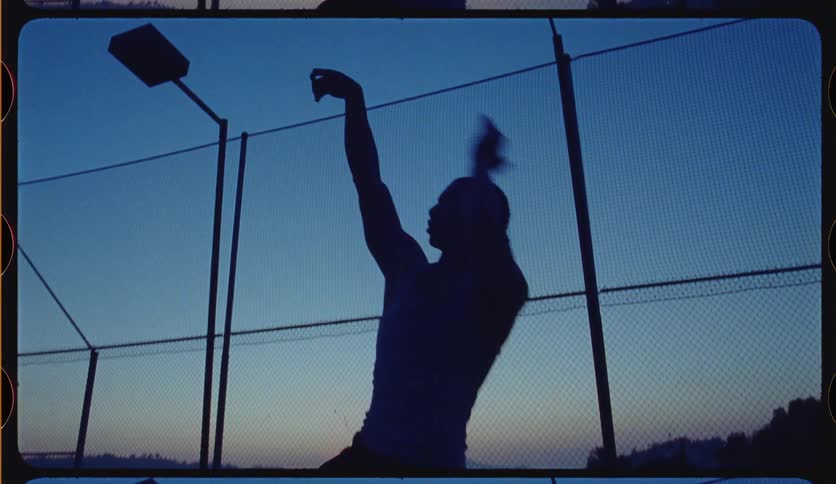 A cinematic slow-motion shot shows a basketball player's silhouette as they take a jump shot at twilight on an outdoor court