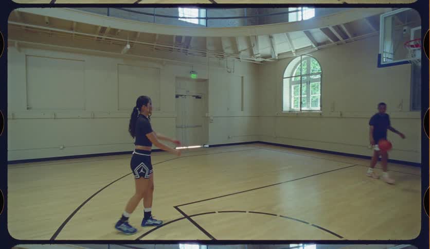 A young man and woman practice basketball in slow motion on a vintage indoor court, passing and shooting hoops