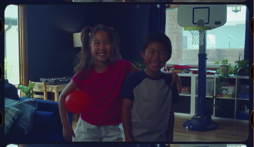 A joyful brother and sister laugh happily for the camera in their playroom, presented in a nostalgic, vintage film style
