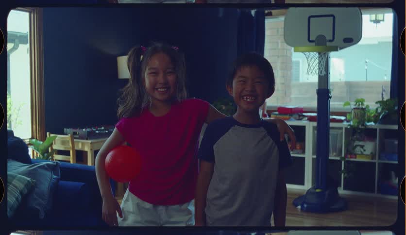 A vintage-style film recording captures two happy Asian siblings smiling and posing in their playroom