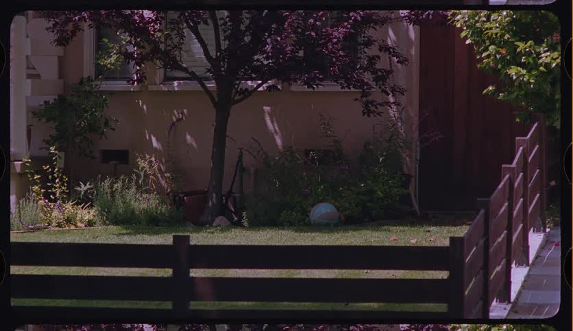 Vintage film frame captures a tranquil suburban front yard with a child's ball resting on the manicured lawn