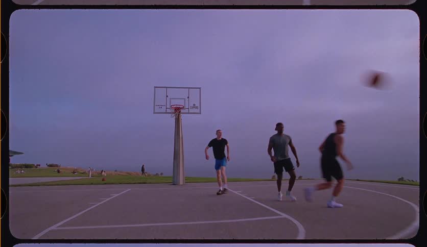 Friends play a pickup basketball game on an outdoor court at dusk, ending with a successful layup in slow motion with a vintage film look