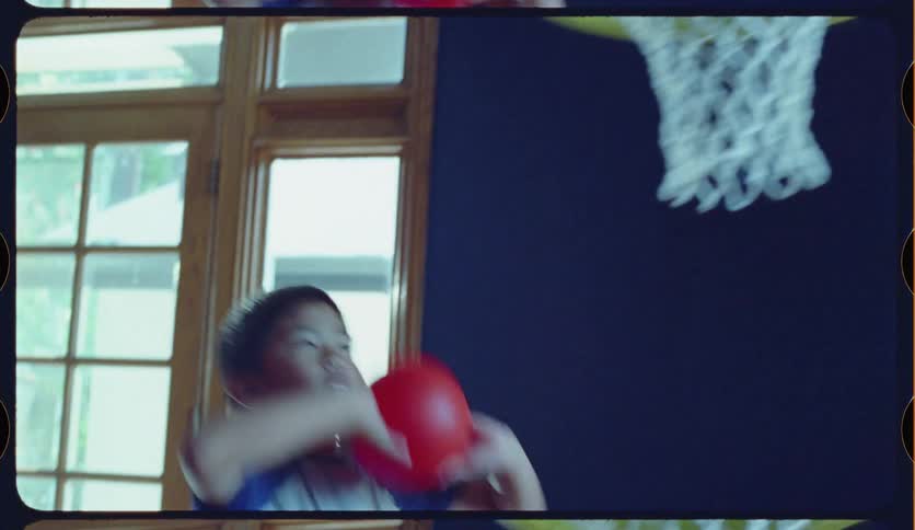 Happy Asian siblings play basketball in slow motion in their living room, passing the ball and making a basket in a toy hoop
