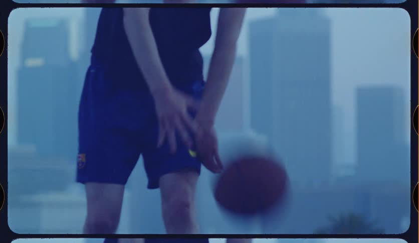 Vintage film-style slow motion shot of a young man dribbling a basketball on a city court against a hazy skyline