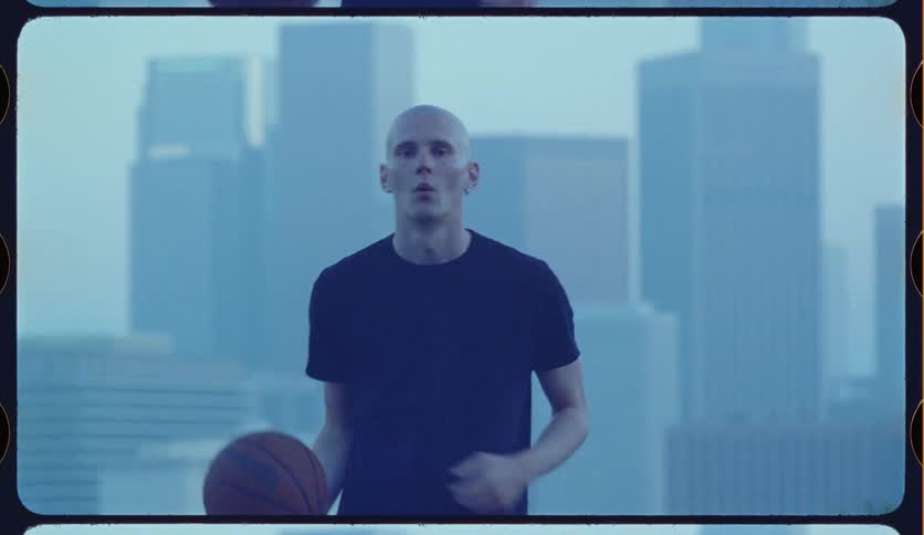 Stylized slow-motion footage of a bald man handling a basketball with a hazy downtown Los Angeles skyline in the background