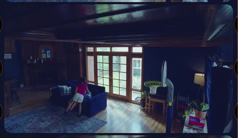 A brother and sister playfully compete in a game of basketball inside their living room in this home video-style clip