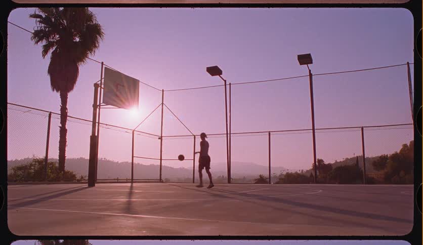 A lone basketball player practices shooting hoops in slow motion on a picturesque outdoor court at sunset
