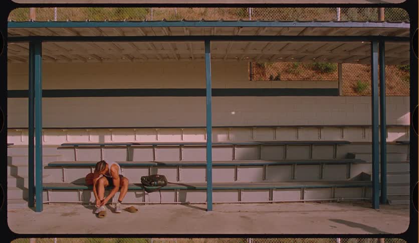 A solitary young basketball player sits alone on empty bleachers, looking tired and contemplative