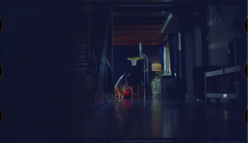 A young brother and sister play with a toy basketball and hoop in a dimly lit hallway at home