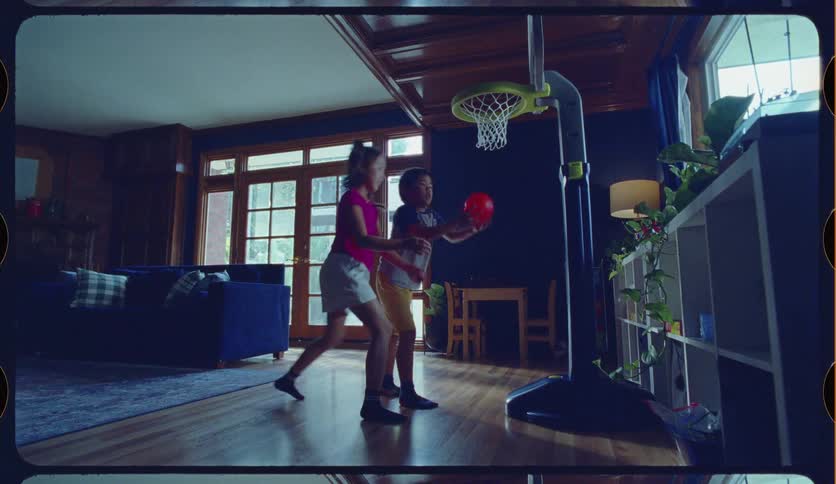 Nostalgic home movie footage shows a brother and sister running into the living room to play with a toy basketball hoop