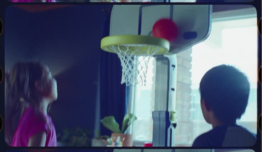 Slow motion footage with a nostalgic film look shows a young Asian brother and sister having fun playing basketball indoors
