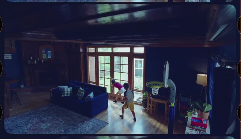 Slow motion shot of two young children happily playing with a toy basketball and hoop in their living room