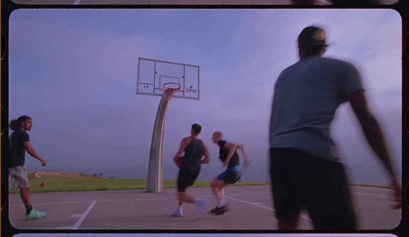 In slow motion, a group of friends play a game of pickup basketball on an outdoor court, ending with a layup shot
