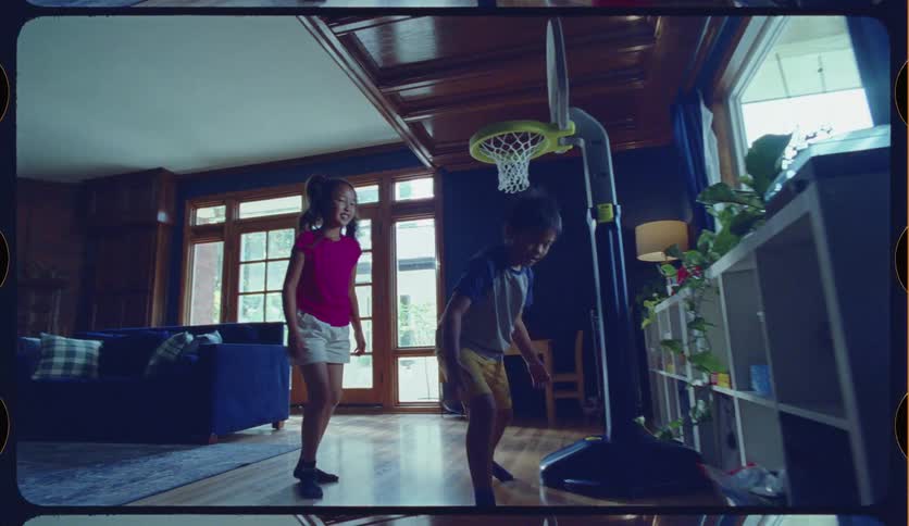Two young children play basketball inside their home in a slow-motion, vintage-style home movie