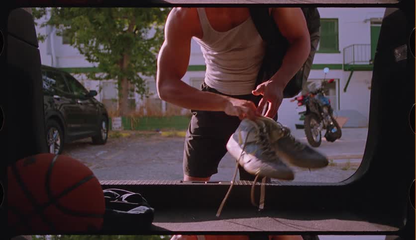 Shot from inside a car's trunk, a young athletic man opens the hatch, grabs his basketball gear, and closes it
