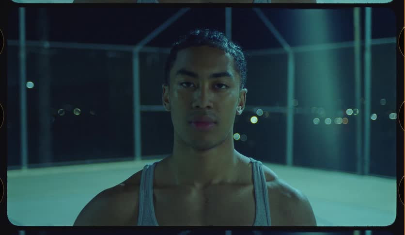 Vintage film style portrait of a focused and muscular young man on an outdoor court at night