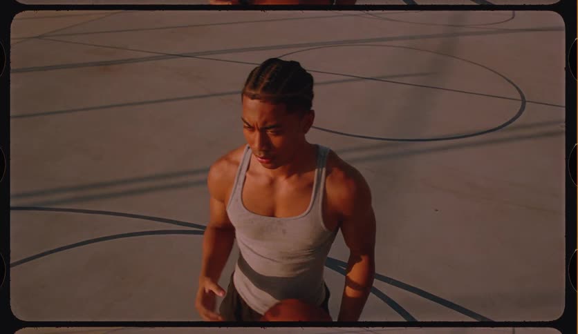 An overhead slow-motion shot of a focused young man dribbling and shooting a basketball on an outdoor court, captured with a vintage film look