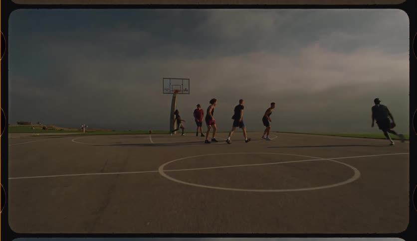 Slow-motion footage with a retro 8mm film look captures a group of friends playing a casual game of basketball on a scenic outdoor court