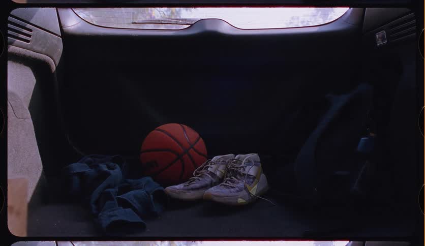 A nostalgic, filmic still life of a basketball and well-worn sneakers in the back of a car as sunlight shifts and changes