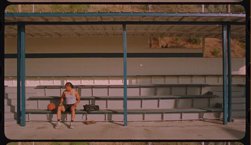 A lone male basketball player stretches and contemplates while sitting on empty bleachers before a game