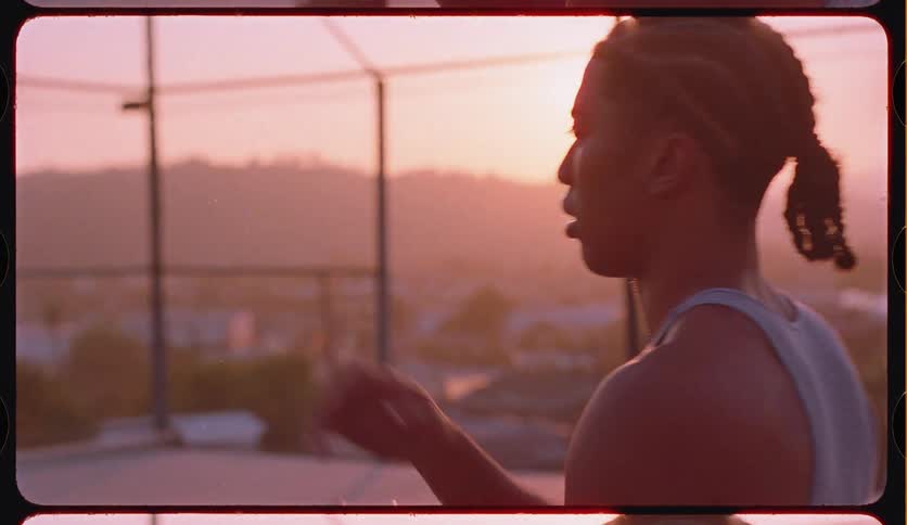 A determined young man practices his basketball skills, dribbling and shooting on an outdoor court during a hazy golden hour sunset