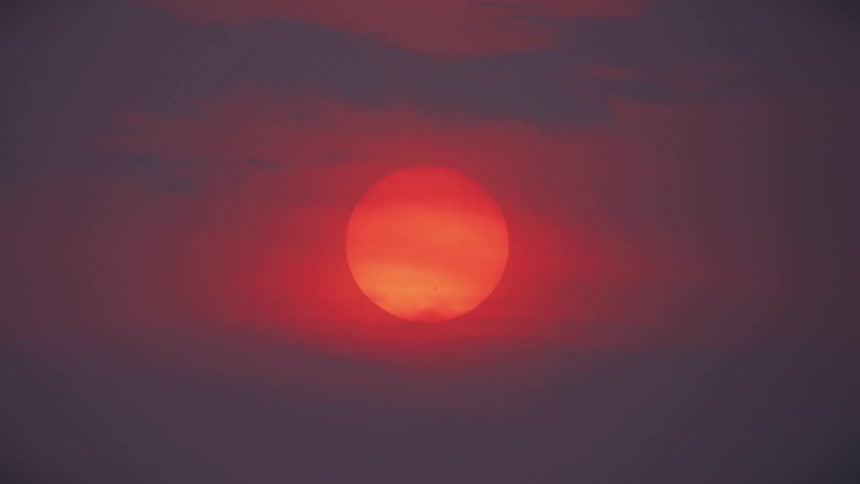 A dramatic close-up shot of a vibrant red sun setting in a hazy, purple sky