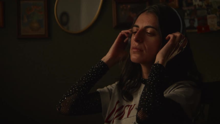 A woman with an alternative style puts on her headphones and relaxes while listening to music in her dark and cozy room