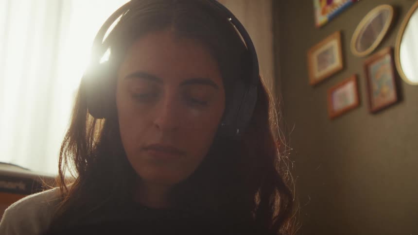 A close-up of a relaxed woman meditating with headphones on in her cozy, sunlit room