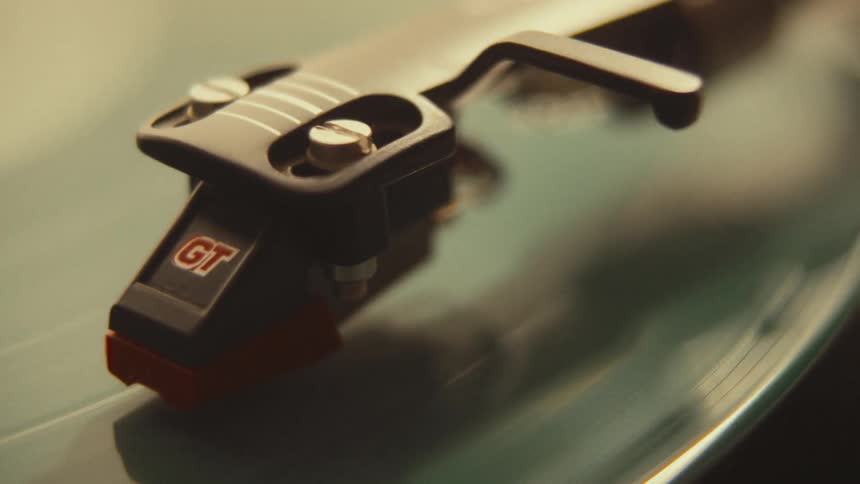 A moody close-up shot of a record player stylus on a spinning green vinyl record