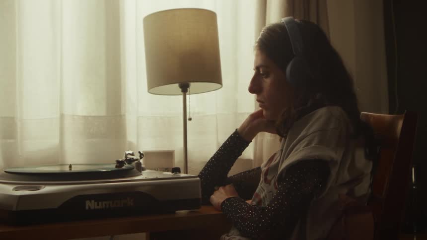 A young woman wearing headphones sits pensively at her desk, listening to music from a vinyl record player