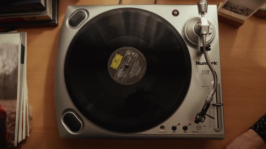 A black vinyl LP album spins on a silver record player, seen from a top-down perspective on a wooden desk