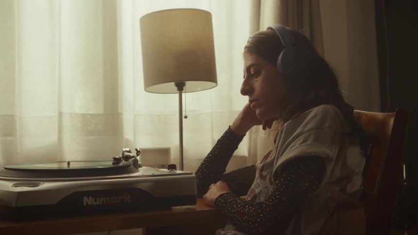 A woman in headphones sits thoughtfully by a window, listening to music from a spinning vinyl record on a turntable