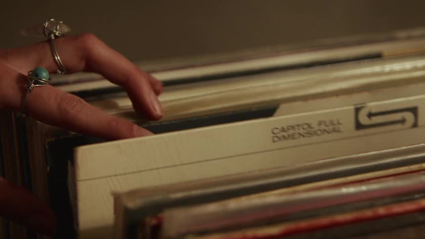 A close-up shot of a hand adorned with rings slowly flipping through a collection of old vinyl records