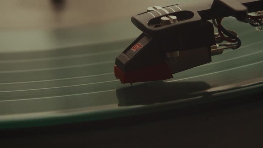 A tight close-up shot of a record player's stylus moving along the grooves of a spinning green vinyl record