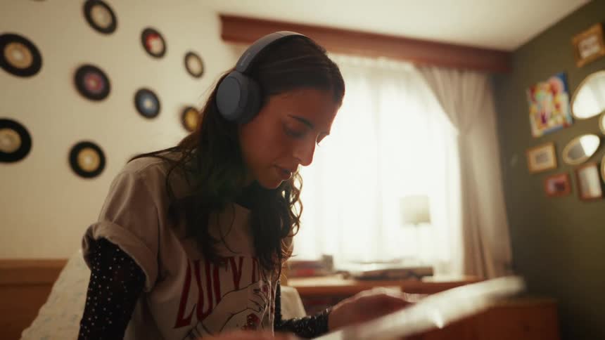 Close-up of a young woman enjoying her vinyl record collection while listening to music on headphones in her bedroom