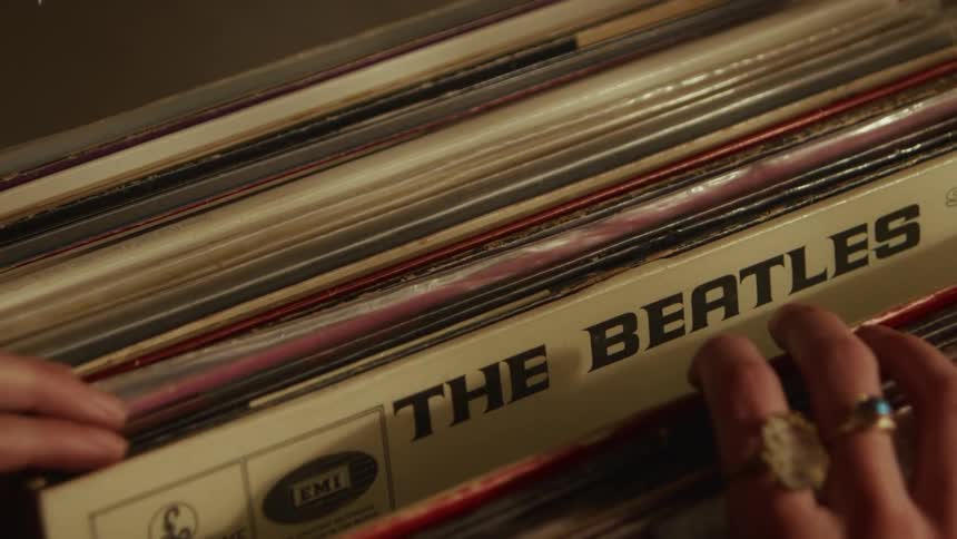 A close-up shot of hands adorned with rings carefully flipping through a collection of classic vinyl records