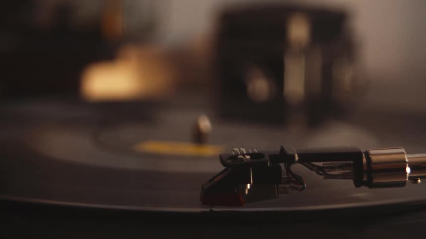 A close-up of a hand placing a stylus on a spinning vinyl record, followed by a detailed shot of the needle playing the music