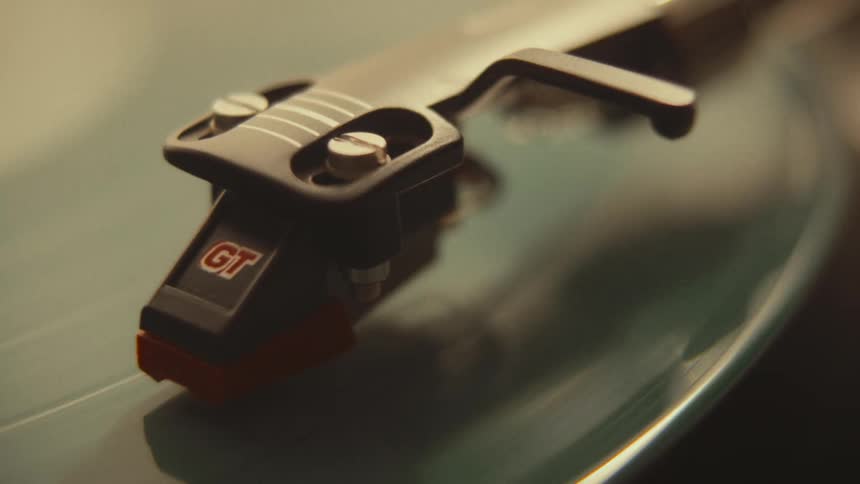 A warm, close-up shot of a turntable stylus playing a spinning teal-colored vinyl record