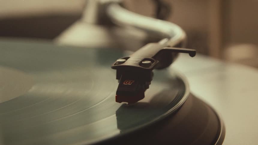 A close-up slow-motion shot of a hand gently lowering the stylus onto a spinning vinyl record