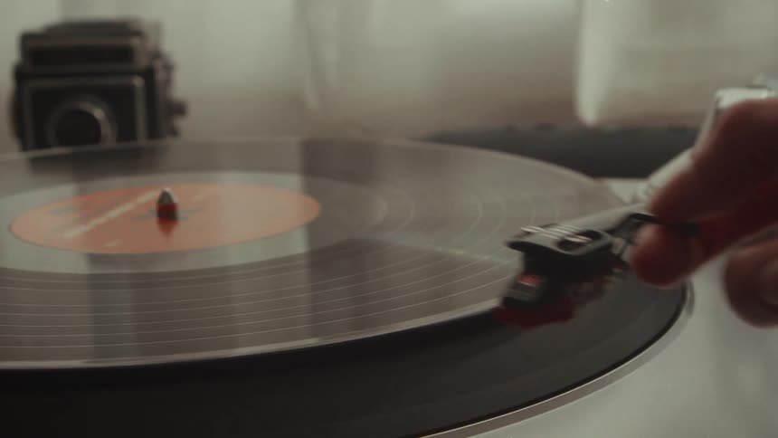 A person lifts the needle off of a spinning vinyl record in slow motion