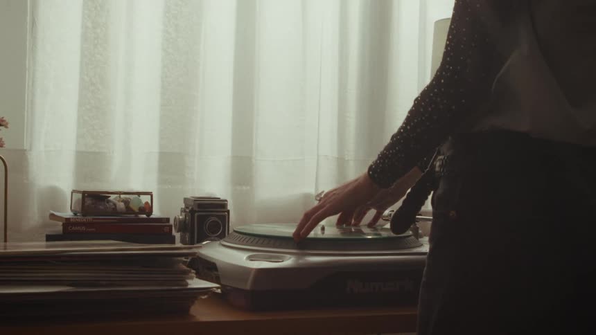 A person carefully places a green vinyl record onto a turntable to play music in a cozy, softly lit room