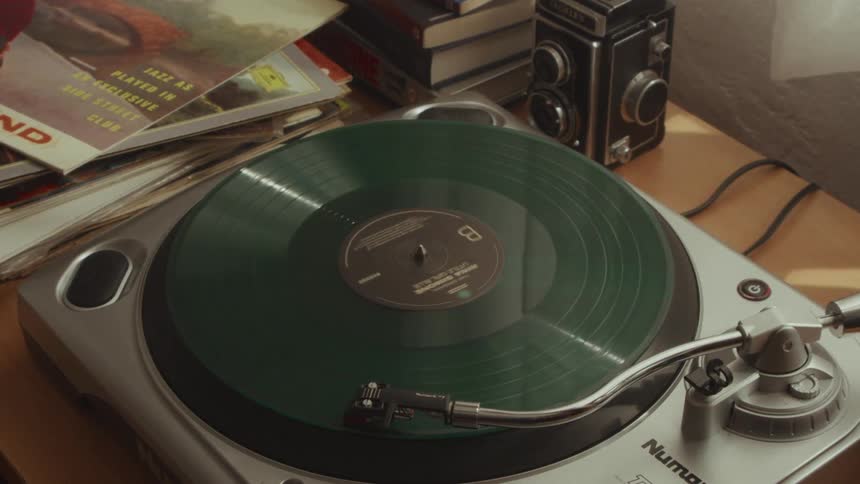 A green vinyl record spins on a turntable, evoking a nostalgic mood with a vintage camera and old magazines nearby