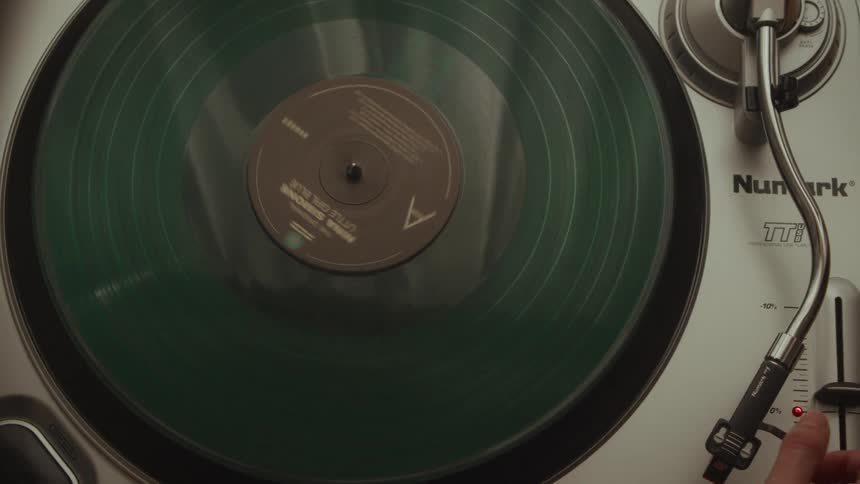 Top-down shot of a woman's hands starting a green vinyl record of Nina Simone's 'Little Girl Blue' on a turntable
