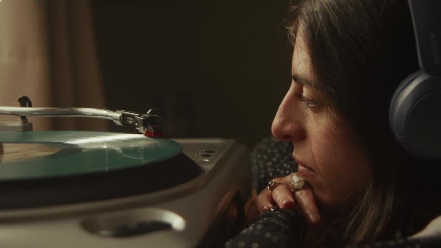 A woman wearing headphones carefully puts the needle on a spinning vinyl record and listens to the music