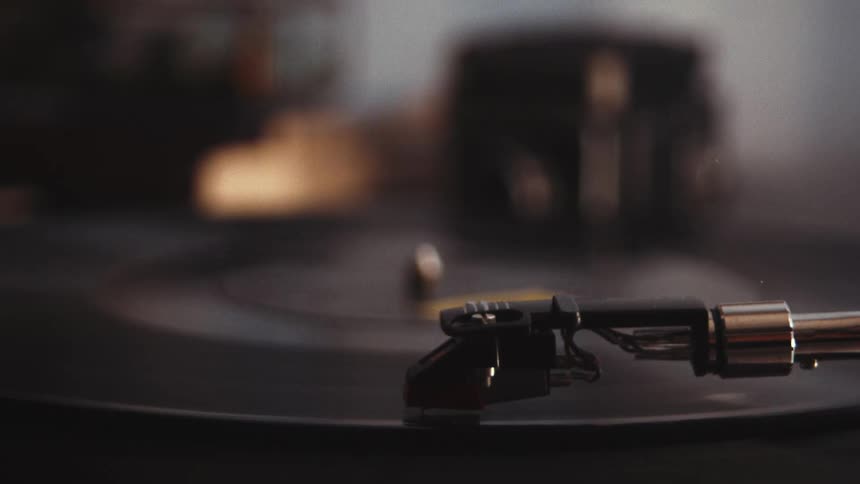 A vintage record player spins a classic vinyl record, with the camera focus pulling to the stylus as it plays