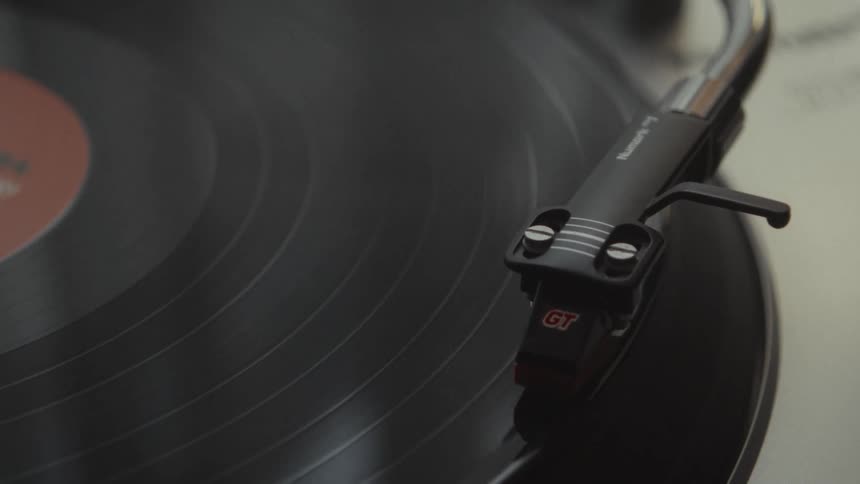 A hand gently lowers the needle onto a spinning vinyl record in a cinematic close-up